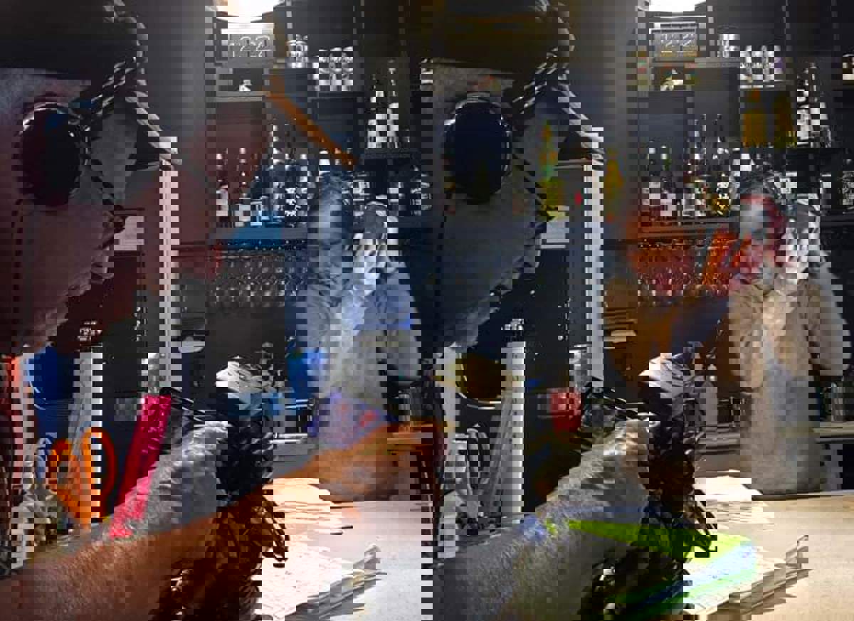 A woman shakes a cocktail behind a bar while a filmmaker films