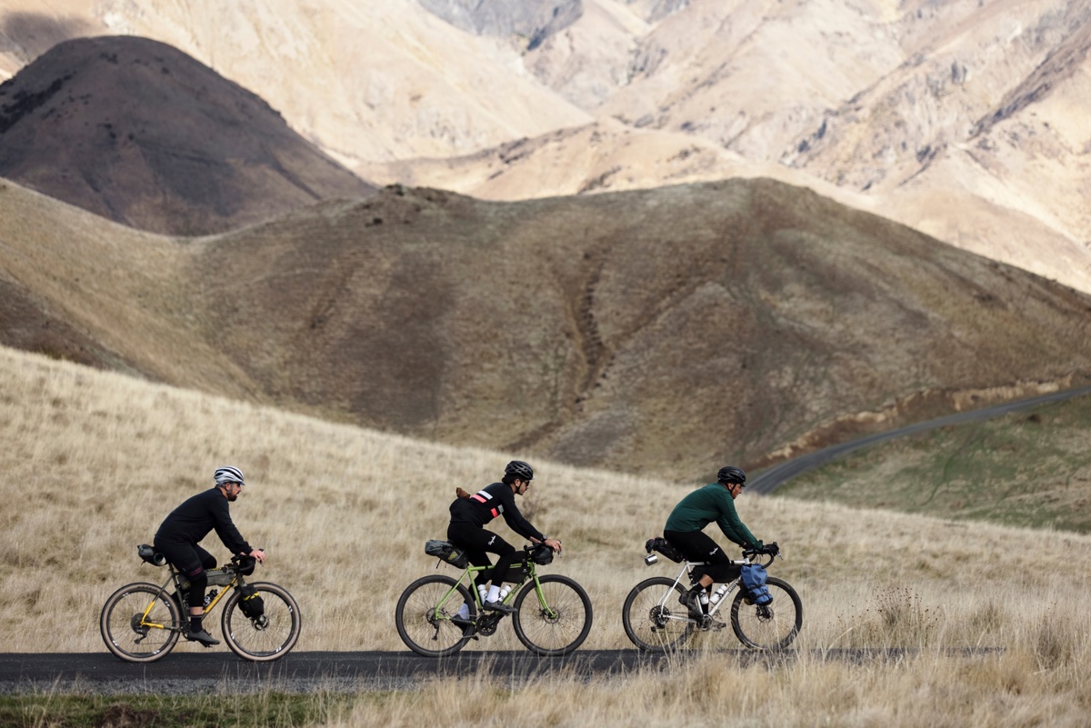 Three cyclists riding in Marlborough against a background of tussock-clad hills