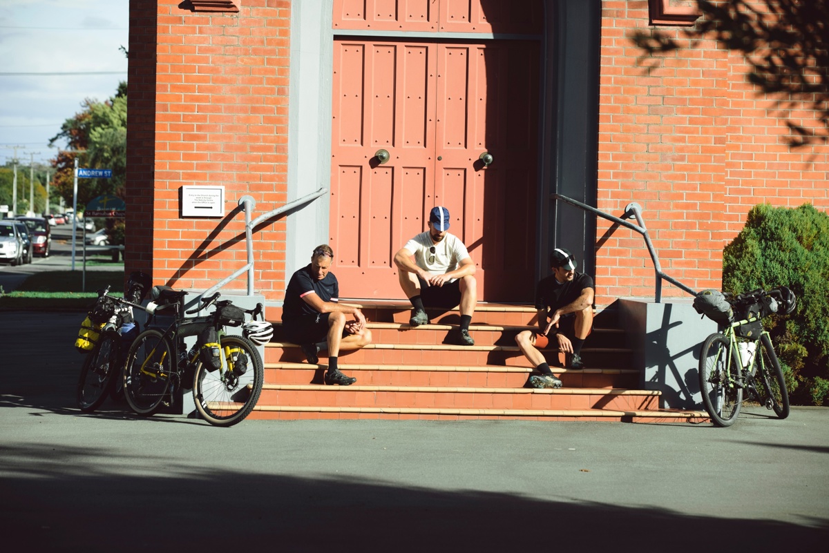 Three cyclists taking a break, sitting in the sunshine on steps outside a church