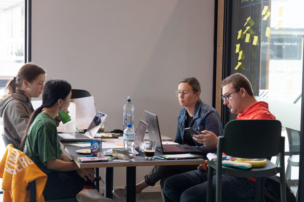 A small group sits at a table with laptops and notepads